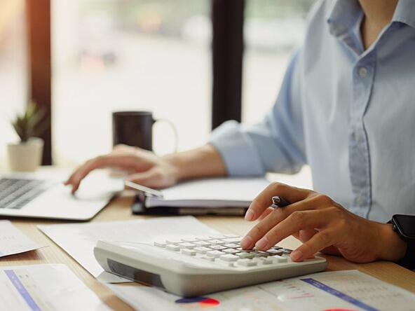 person calculating budget using calculator and laptop while seated at desk